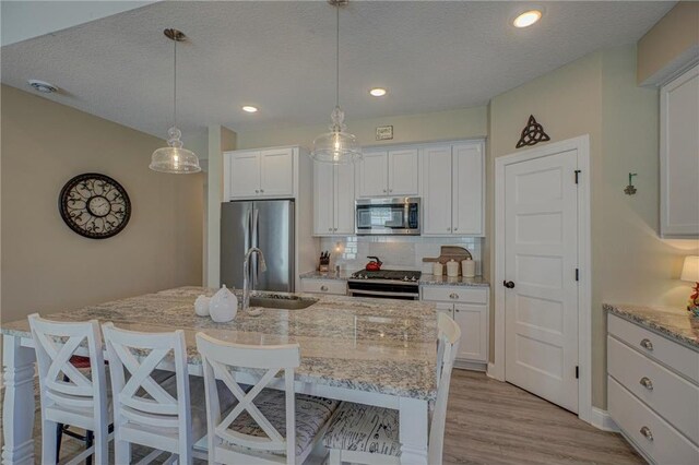 102 Linden Ave, Hudson, WI 54016 - kitchen featuring a sink, a breakfast bar area, stainless steel appliances, a kitchen island with sink, and white cabinets