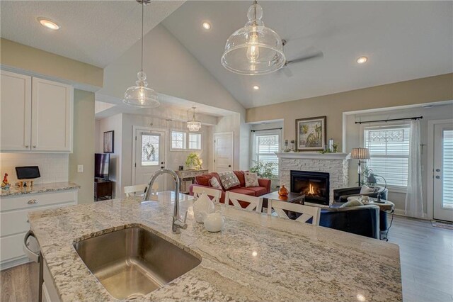 102 Linden Ave, Hudson, WI 54016 - kitchen featuring white cabinets, light wood-style flooring, a stone fireplace, a sink, and open floor plan