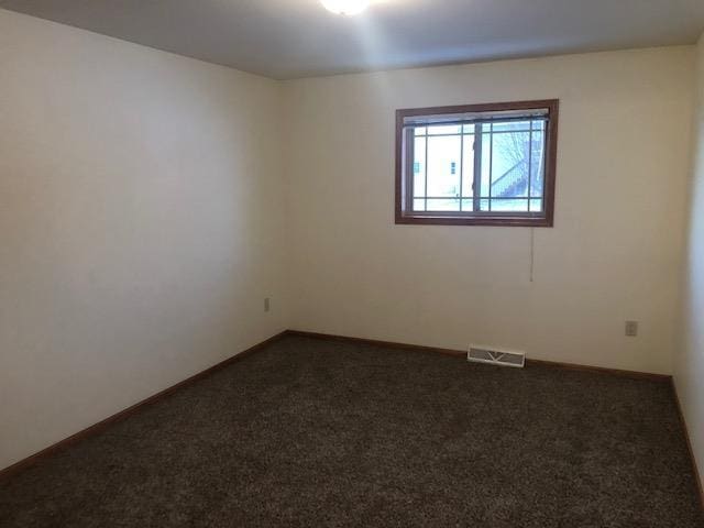 spare room with dark carpet, visible vents, and baseboards