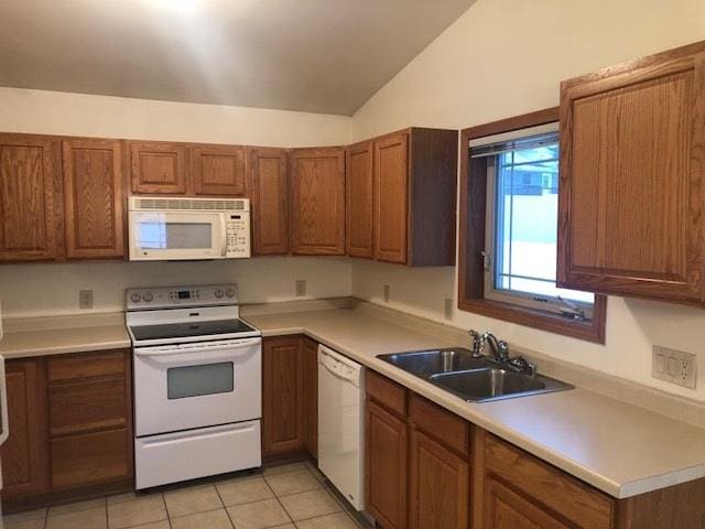 kitchen featuring brown cabinets, lofted ceiling, light countertops, a sink, and white appliances