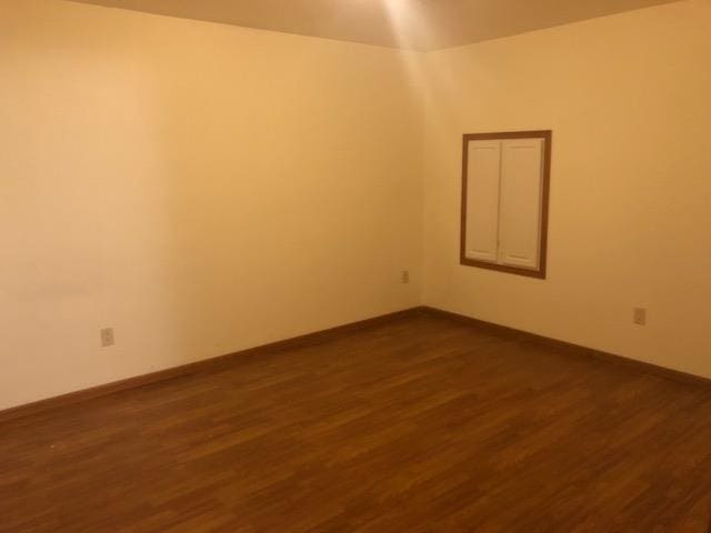 empty room featuring baseboards and dark wood finished floors