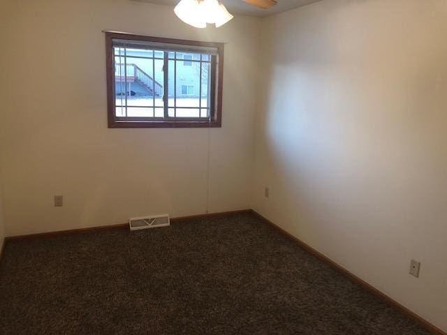 empty room featuring dark carpet, ceiling fan, baseboards, and visible vents