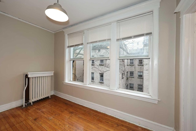 spare room with radiator, hardwood / wood-style flooring, ornamental molding, and baseboards