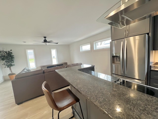 kitchen featuring a kitchen bar, a healthy amount of sunlight, stainless steel fridge with ice dispenser, and wall chimney range hood