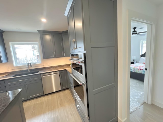 kitchen featuring gray cabinetry, light wood-style floors, dark stone counters, stainless steel dishwasher, and a sink