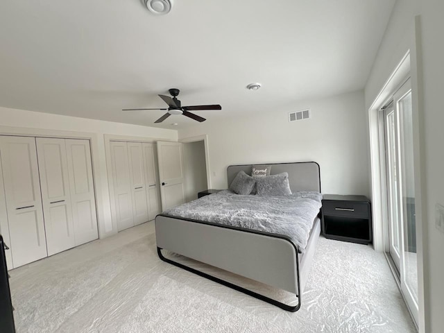 bedroom featuring visible vents, light colored carpet, two closets, and a ceiling fan