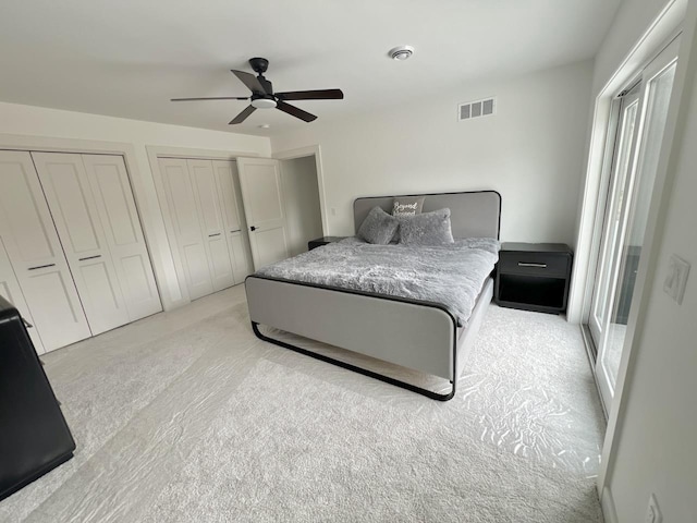 bedroom featuring visible vents, light colored carpet, multiple closets, and ceiling fan