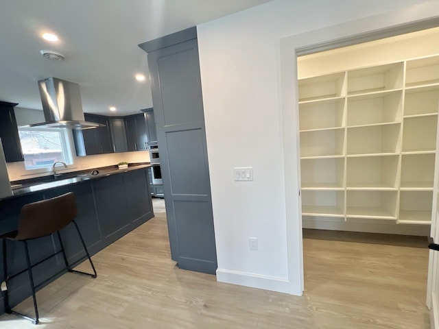 kitchen featuring light wood-style flooring, recessed lighting, island exhaust hood, stainless steel double oven, and baseboards