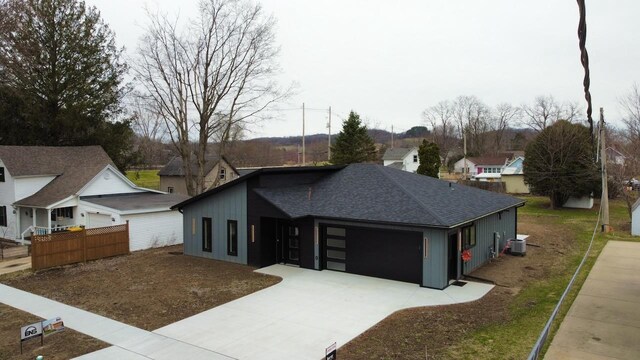 view of front of home with a shingled roof, an attached garage, fence, cooling unit, and driveway