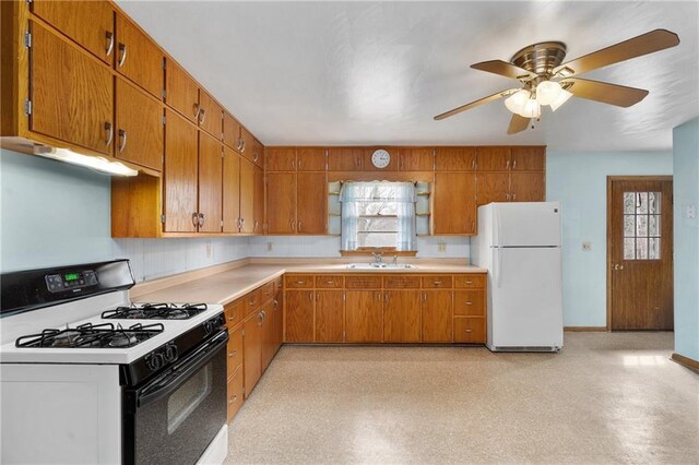 kitchen featuring gas range oven, under cabinet range hood, a sink, freestanding refrigerator, and brown cabinets