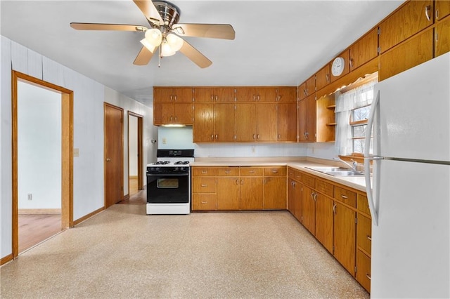 kitchen featuring light countertops, range with gas stovetop, a sink, brown cabinetry, and freestanding refrigerator