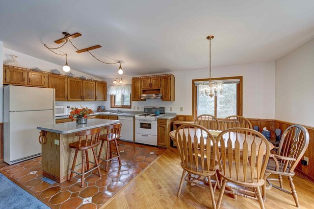 W5854 Bubbling Springs Dr, Elkhorn, WI 53121 - kitchen featuring an inviting chandelier, white appliances, brown cabinetry, a kitchen island, and under cabinet range hood