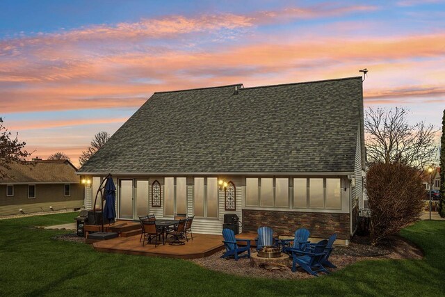 119 Vilas Hibbard Pkwy, Lodi, WI 53555 - back of property at dusk featuring stone siding, a patio, a lawn, a shingled roof, and a fire pit