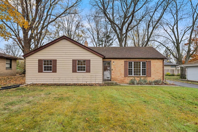 ranch-style home with a shingled roof, a chimney, brick siding, and a front yard
