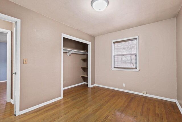 unfurnished bedroom featuring baseboards, wood finished floors, and a closet