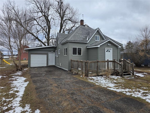 view of front of house featuring a garage, a chimney, a wooden deck, driveway, and roof with shingles