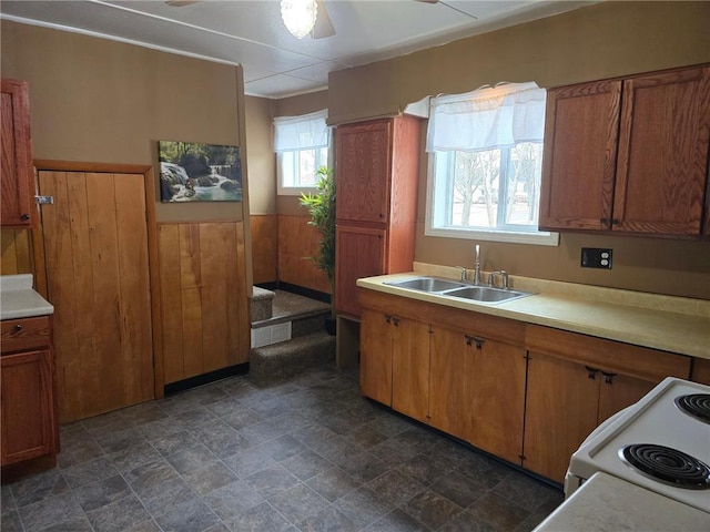 kitchen featuring a sink, light countertops, ceiling fan, white electric range oven, and stone finish flooring