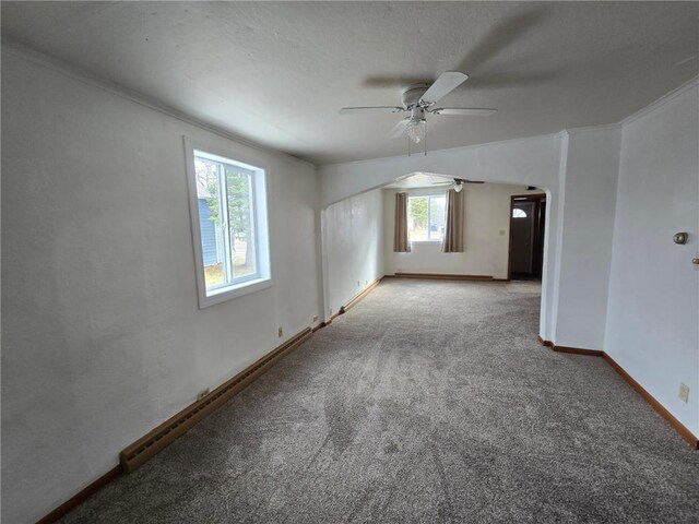 empty room featuring carpet floors, a wealth of natural light, a ceiling fan, and arched walkways