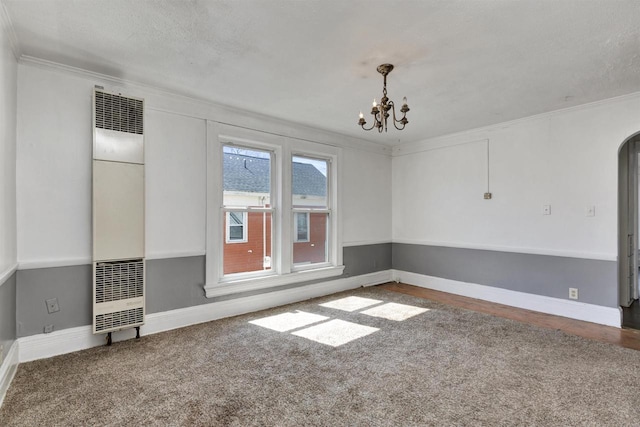 carpeted spare room featuring crown molding, arched walkways, a heating unit, and a notable chandelier