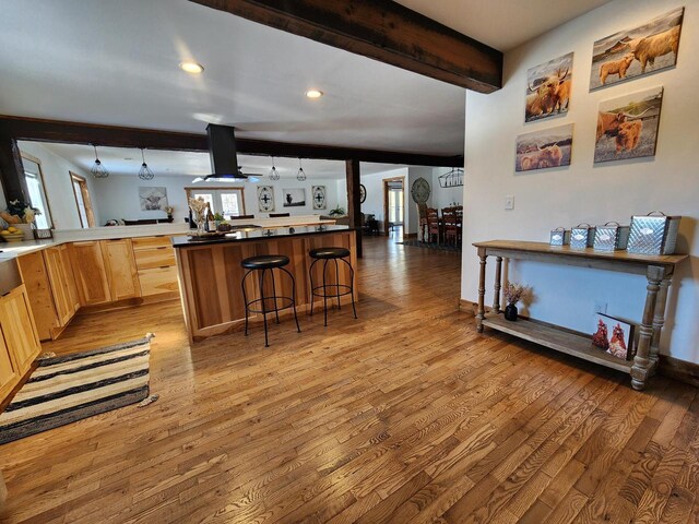 26350 Drake Ln, Cazenovia, WI 53924 - kitchen with island exhaust hood, a kitchen bar, beam ceiling, light wood-style floors, and light brown cabinetry