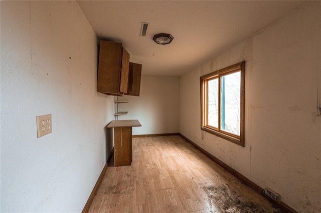interior space with baseboards, light wood-style floors, a textured ceiling, and visible vents