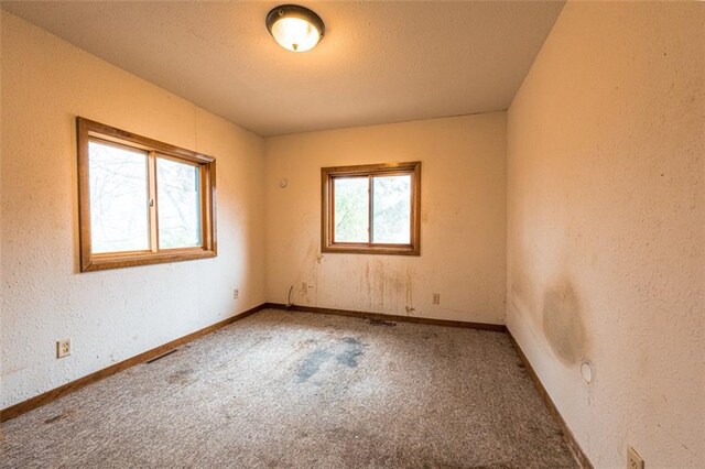unfurnished room with carpet floors, a textured wall, baseboards, and a textured ceiling