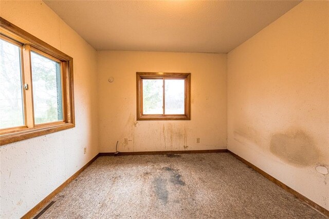 empty room featuring carpet flooring, plenty of natural light, baseboards, and visible vents