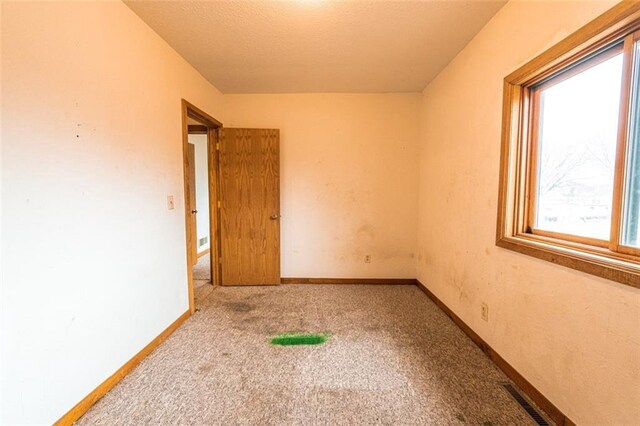 carpeted spare room with baseboards, a textured ceiling, and visible vents
