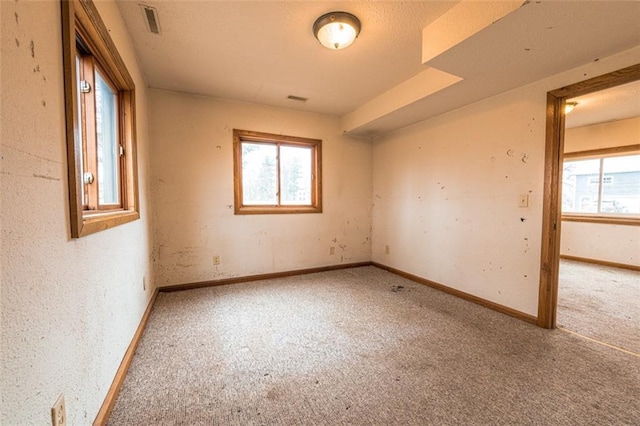 unfurnished room with baseboards, visible vents, carpet, and plenty of natural light
