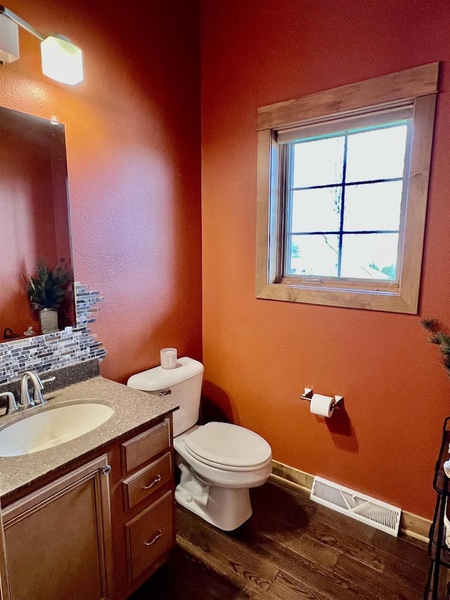 bathroom featuring wood finished floors, vanity, baseboards, toilet, and visible vents