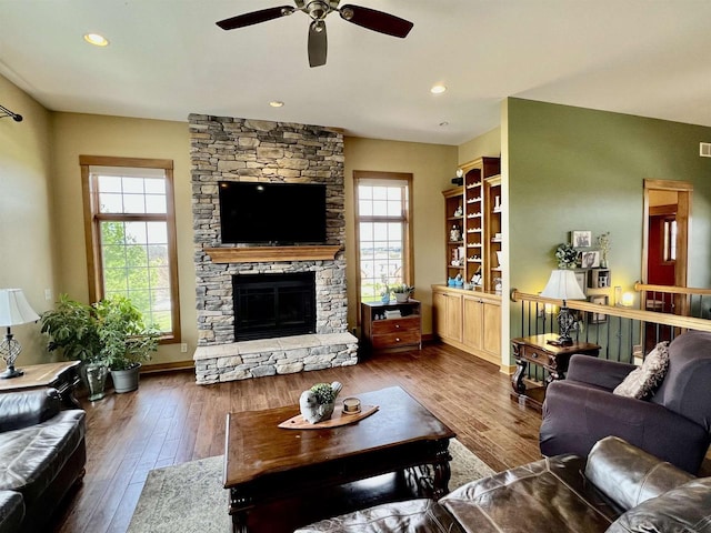 living area featuring baseboards, recessed lighting, ceiling fan, hardwood / wood-style floors, and a stone fireplace