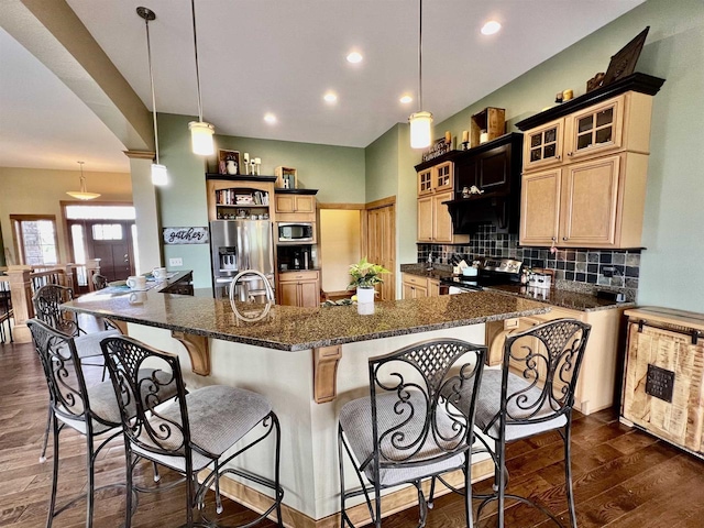 kitchen with a sink, a breakfast bar, appliances with stainless steel finishes, backsplash, and dark wood-style flooring
