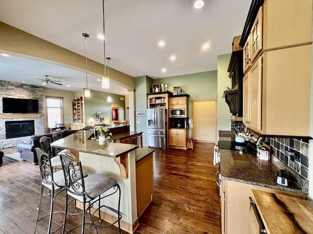 kitchen featuring a breakfast bar, ceiling fan, stainless steel appliances, a fireplace, and dark wood-type flooring