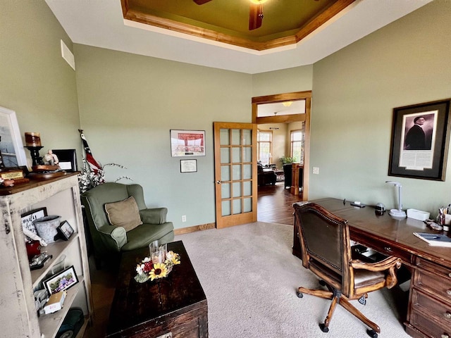 carpeted home office featuring a raised ceiling, baseboards, and french doors