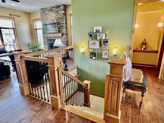 stairway featuring a stone fireplace, a ceiling fan, wood finished floors, and baseboards