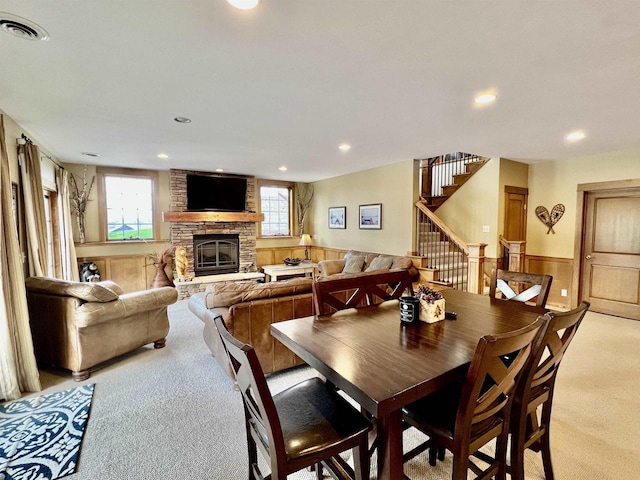 dining space with stairs, a stone fireplace, wainscoting, light colored carpet, and visible vents