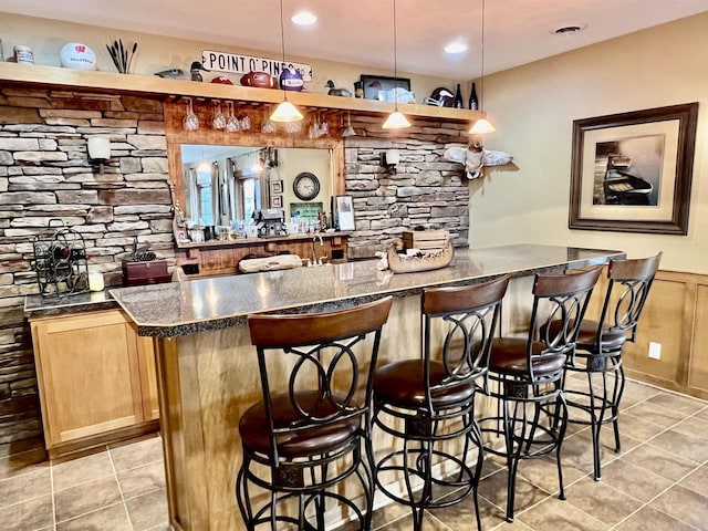 bar featuring light tile patterned flooring, decorative light fixtures, and a wainscoted wall