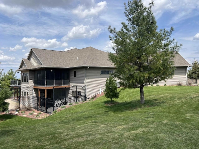 rear view of property with roof with shingles, a sunroom, and a yard