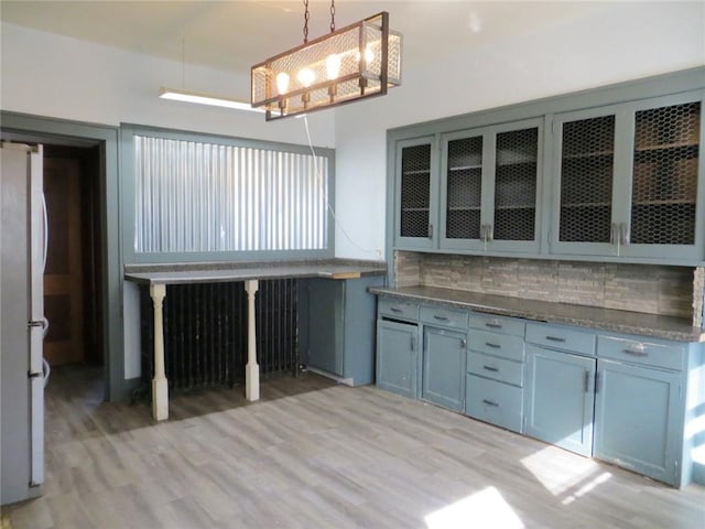 204 W Main St, Thorp, WI 54771 - kitchen with light wood-style flooring, tasteful backsplash, glass insert cabinets, an inviting chandelier, and freestanding refrigerator
