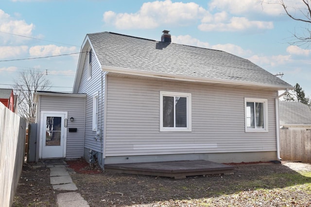 back of property featuring a chimney, a deck, fence, and roof with shingles