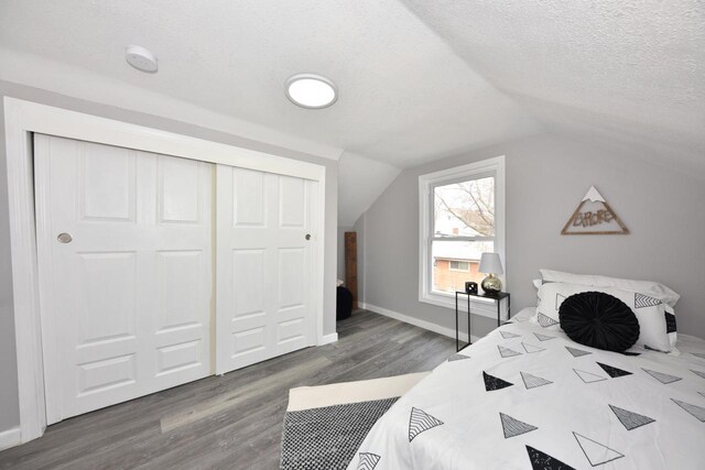 bedroom with lofted ceiling, baseboards, a textured ceiling, a closet, and wood finished floors