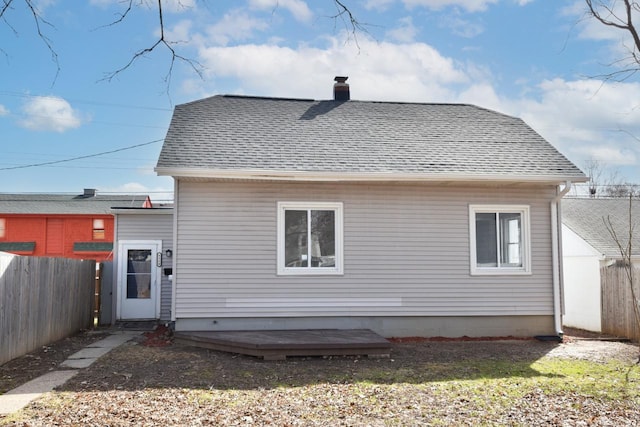 back of house featuring a shingled roof, fence, and a chimney