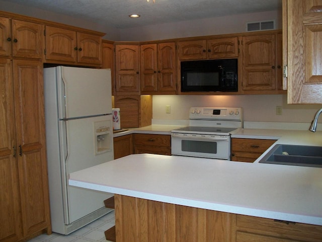 kitchen featuring visible vents, a peninsula, white appliances, brown cabinets, and a sink