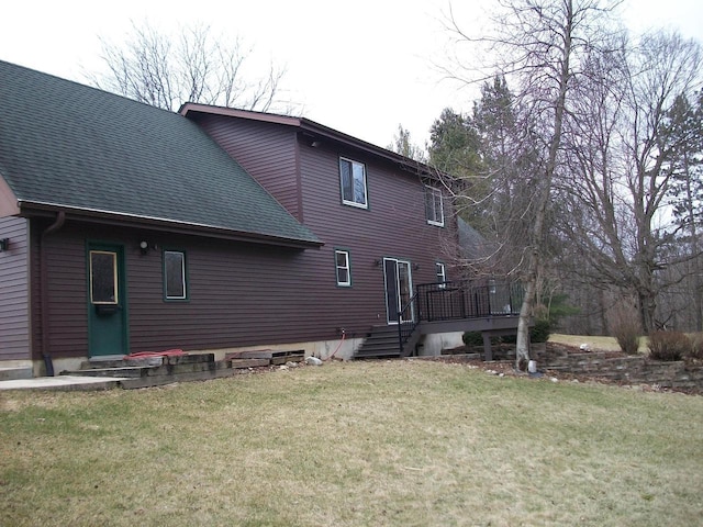 rear view of house featuring a lawn, a wooden deck, entry steps, and roof with shingles