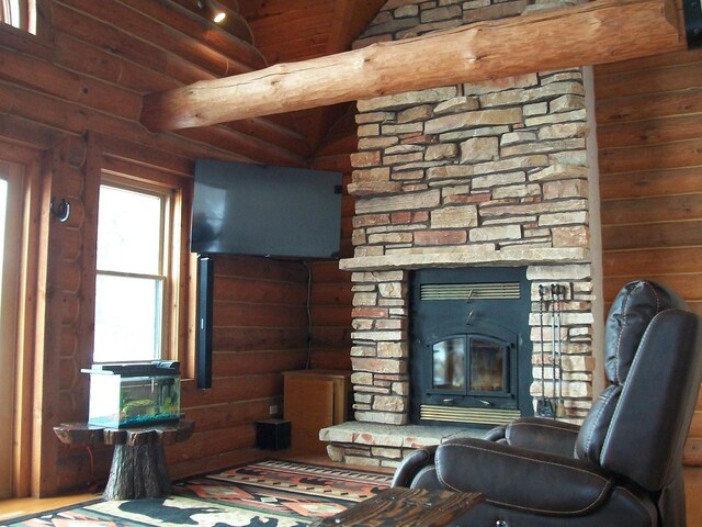 living area featuring a stone fireplace, beamed ceiling, and rustic walls