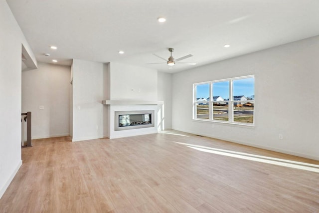 6608 Grouse Woods Rd, Deforest, WI 53532 - unfurnished living room featuring light wood-style flooring, baseboards, ceiling fan, recessed lighting, and a glass covered fireplace