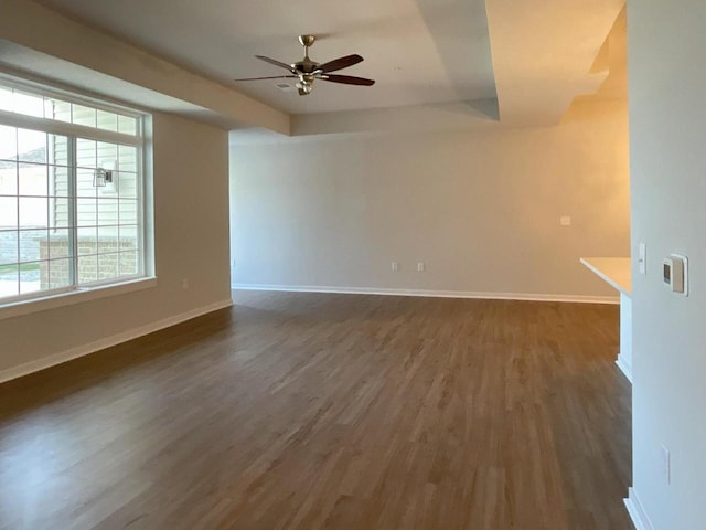spare room with baseboards, dark wood-style flooring, a tray ceiling, and ceiling fan