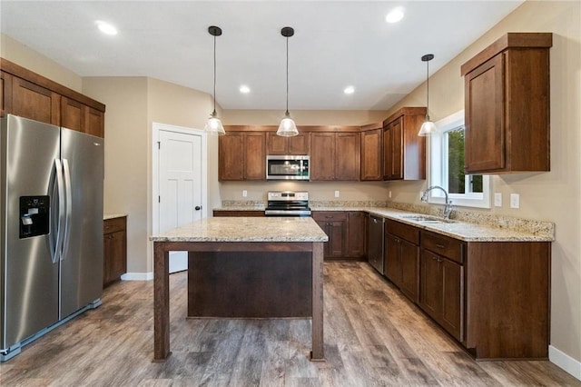 kitchen with light stone countertops, stainless steel appliances, pendant lighting, a sink, and wood finished floors