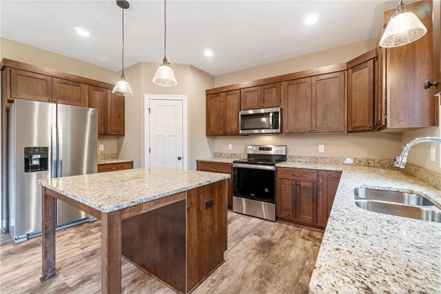 kitchen with a center island, a sink, appliances with stainless steel finishes, light wood finished floors, and light stone countertops