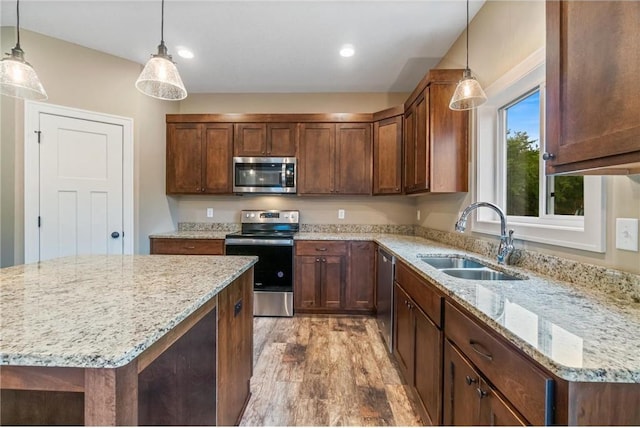 kitchen featuring decorative light fixtures, a sink, light stone countertops, light wood-style flooring, and stainless steel appliances